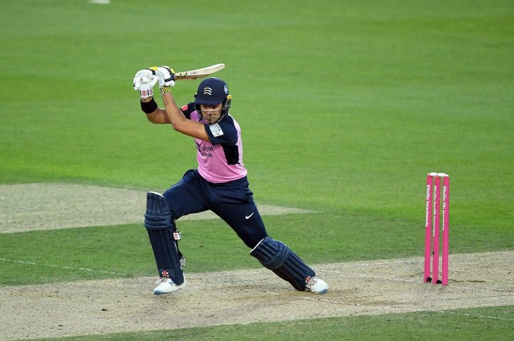 Middlesex left-handed batter Max Holden plays a drive. He is wearing Middlesex's one-day kit: pink shirt with blue sleeves, blue trousers, pads and helmet, with white batting shoes and batting gloves.