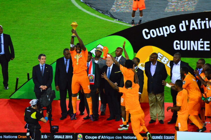 Yaya Toure hosts the AFCON trophy to the sky from the winners podium. He wears the Ivory Coast's iconic orange kit.
