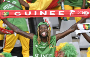 A Guinea fan, smile beaming, holds a banner with his country's name at AFCON 2023