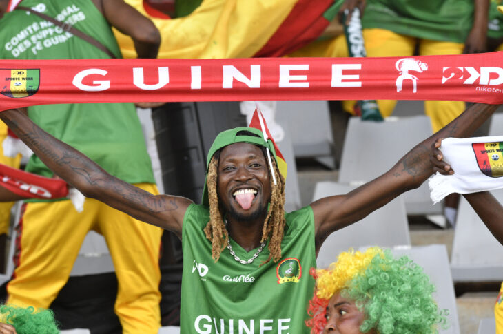 A Guinea fan, smile beaming, holds a banner with his country's name at AFCON 2023