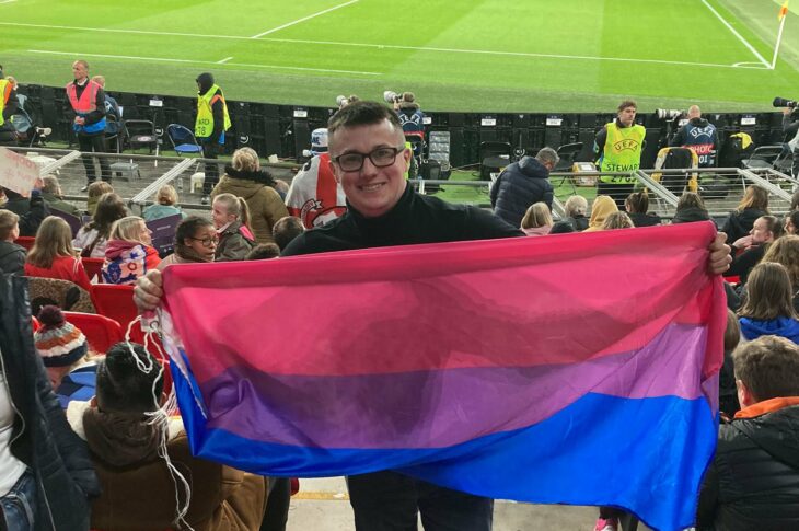 Michael McCann holds up the bisexual flag while in the crowd of a football stadium