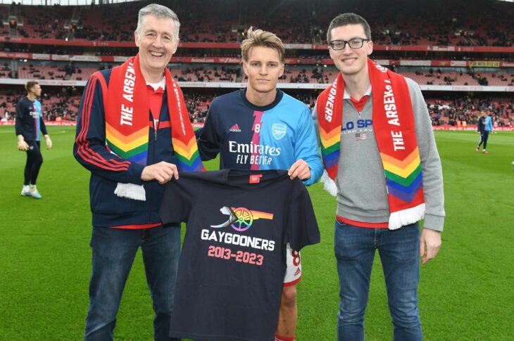 Arsenal captain Martin Odegaard with Carl Fearn and Jacob Jefferson of GayGooners on the Emirates pitch holding a GayGooners t-shirt making Arsenal a safe space