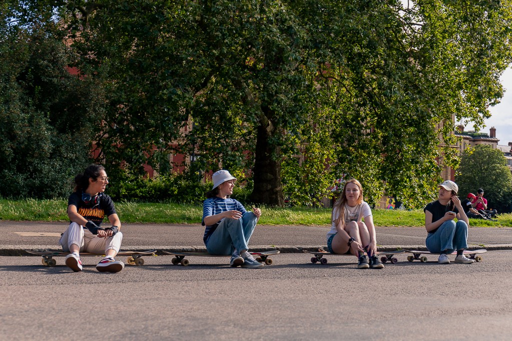 Four longboard skaters sat in a row with their boards