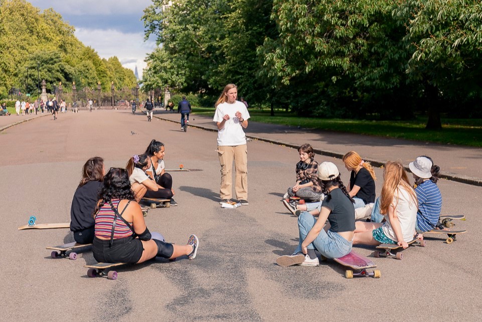 Group of longboard skaters sat in a circle listening to co-leader Imi Thrussell