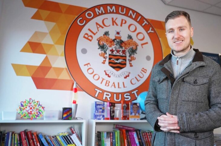 Nick Ransom stands in front of a wall mural showing Blackpool City Community Trust badge.