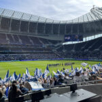 In the Tottenham Hotspur Stadium fans wave blue and white Tottenham flags while the teams line-up on the pitch.