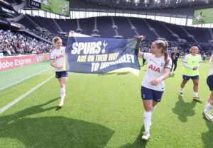 Kit Graham and Luana Buhler parade a banner stating "Spurs are on their way to Wembley" at the Tottenham Hotspur Stadium