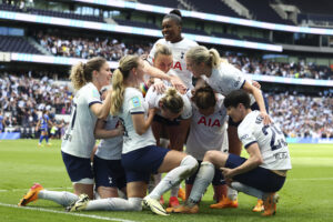 A huddle of Spurs' players join Martha Thomas in celebrating the winning goal. Most are knelt and hug one another.