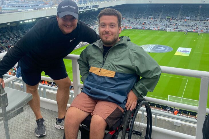 Jack Booth in a wheelchair in the accessible seating area high up in St. James' Park with the pitch and stands in the background.